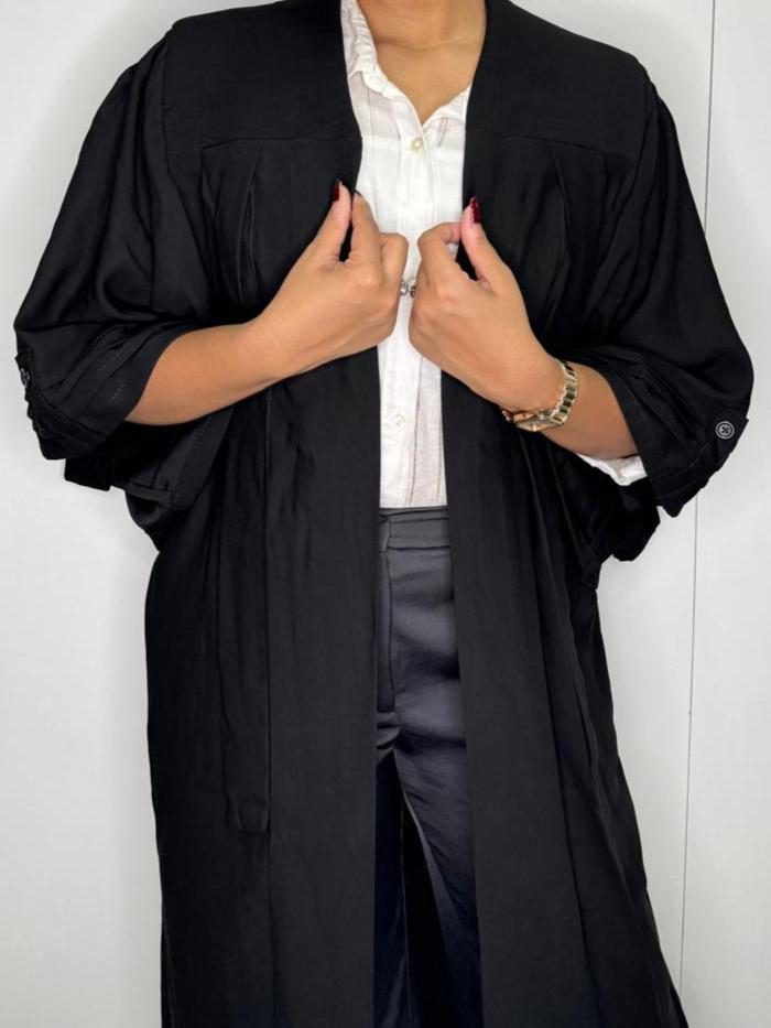 A person wearing a black advocate gown with a white shirt, standing against a white background.